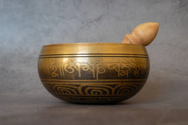 Singing bowl close-up, soothing and meditative. Singing bowl with sanskrit engraving pattern and wooden mallet Isolated on gray background. Symbols of Asia.