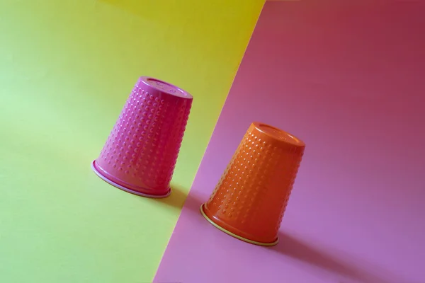 Deux tasses en plastique multicolores inclinées sur un fond jaune et rose. Concept de volatilité des entreprises et de baisse des investissements . — Photo