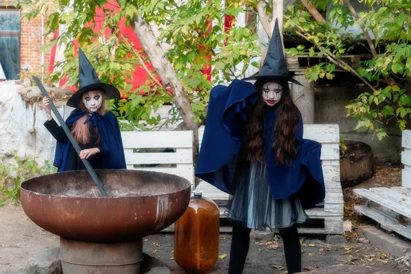 Two little girls in witch costumes brew a magic drink in an aban — Stock Photo, Image