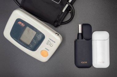 Gri arka planda kan basıncı tonometresi ve Iqos var. Sigara ve ABD'de Iqos elektronik sigara yasağı sağlık zarar kavramı. Rusya, Tataristan, 08 Eylül 2019