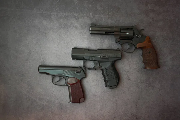 Broń palna ustawiona wzdłuż linii. Trzy pistolety na szarym, betonowym tle. przestrzeń kopiowania — Zdjęcie stockowe