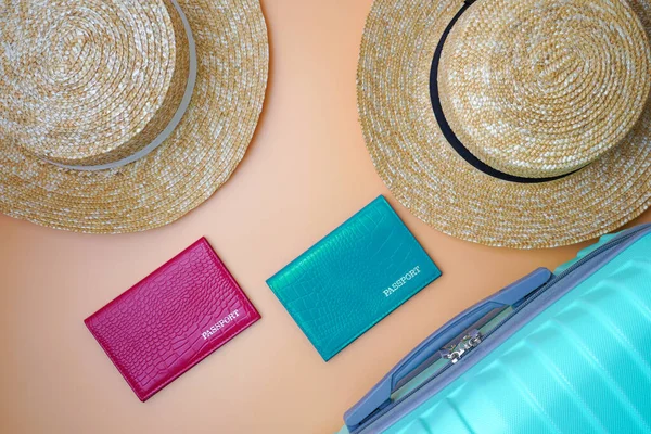 İki kadının plaj hasır şapkaları, pasaportları ve bej arka planda bir bavul. Seyahat, seyahat ve turizm konsepti