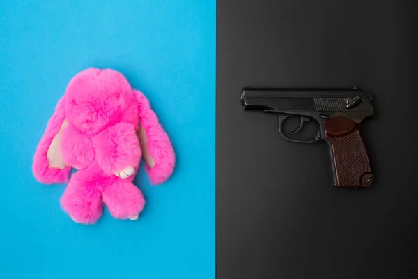 Játék rózsaszín nyúl és fekete pisztoly kék és fekete háttérrel. A gyerekek fegyverviselésének koncepciója az iskolában. Az állatok orvvadászokkal és vadászokkal szembeni védelmének koncepciója — Stock Fotó