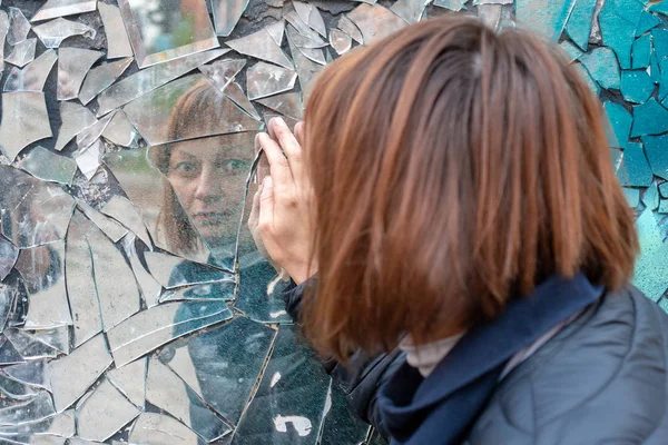 woman looks in a broken mirror and shows her hand on a mirror. T