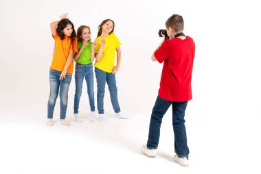 Bir erkek fotoğrafçı stüdyoda beyaz bir arka planda parlak tişörtlü üç tatlı kızın fotoğraflarını çekiyor. Genç fotoğrafçı ve blog yazarı