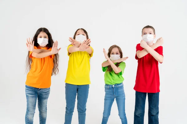 Grupo de escolares niños con coloridas camisetas y máscaras médicas mostrando gesto de las manos cruzadas mientras miran a la cámara sobre fondo blanco. Aislado. Quédate en casa. Decir no a la — Foto de Stock