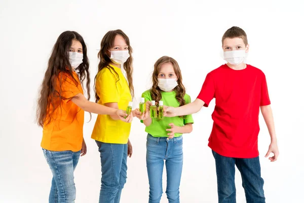 Um grupo de crianças em idade escolar com camisetas brilhantes e máscaras médicas está segurando desinfetantes. Fica em casa e lava-me as mãos. Coronavírus. Temporada de doenças virais . — Fotografia de Stock