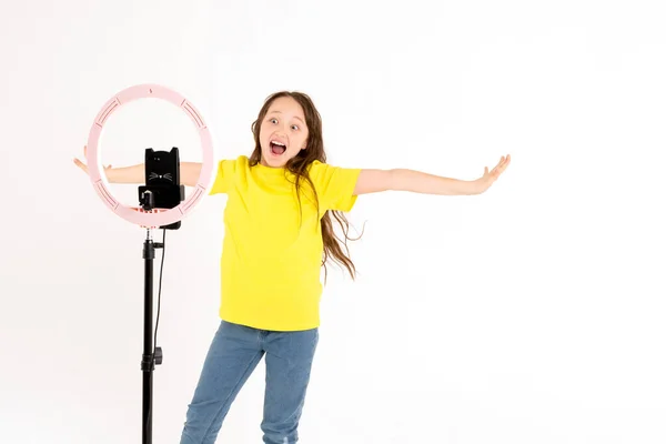 Seorang gadis remaja menari dan syuting video. Selfie. Ponsel dipasang pada tripod dan lampu cincin bersinar. Emosi kegembiraan dan sukacita di wajah seorang anak — Stok Foto