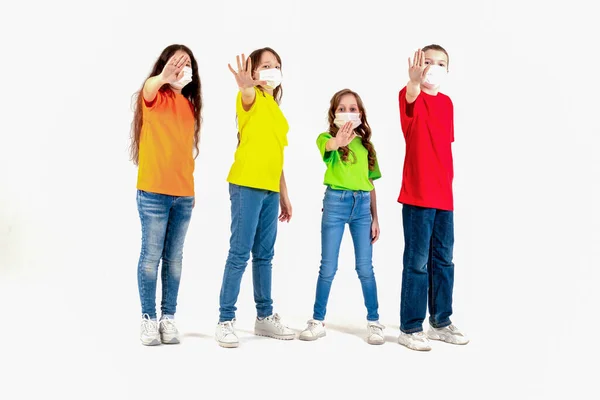 Group of schoolchildren children in colorful T-shirts and medical masks showing crossed hands gesture while looking at the camera over white background. Isolated. Stay at home. Say No to the — Stock Photo, Image