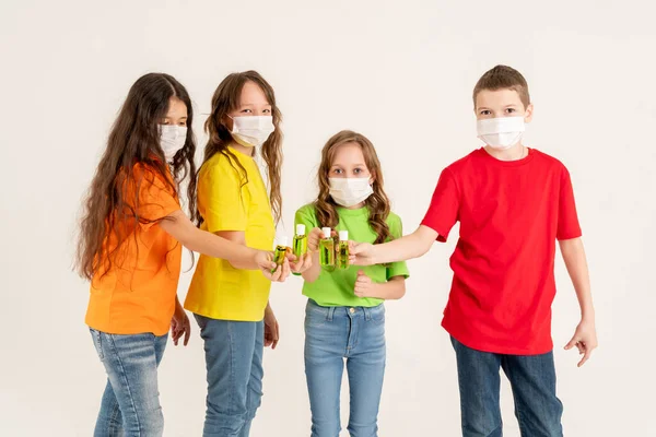Parlak tişörtlü ve tıbbi maskeli bir grup okul çocuğu dezenfektan taşıyor. Evde kal ve ellerimi yıka. Coronavirus. Viral hastalıklar mevsimi. — Stok fotoğraf