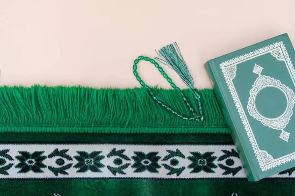 Μουσουλμανική ισλαμική αντίληψη πίστης. Βιβλίο Κοράνι, πράσινο κομπολόι, πράσινο χαλάκι προσευχής. Ουδέτερο μπεζ φόντο. διάταξη και χώρος για κείμενο — Φωτογραφία Αρχείου