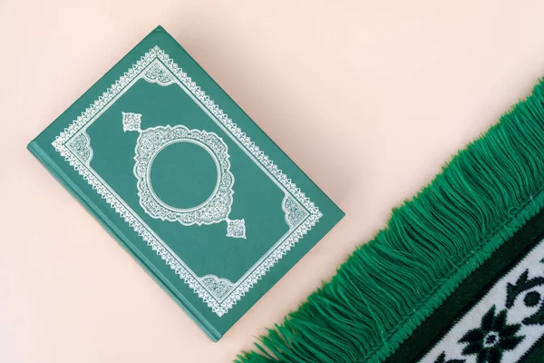 Muslim islamic faith concept Koran book , green rosary, green mat pray . Neutral beige background. layout and Space for text.