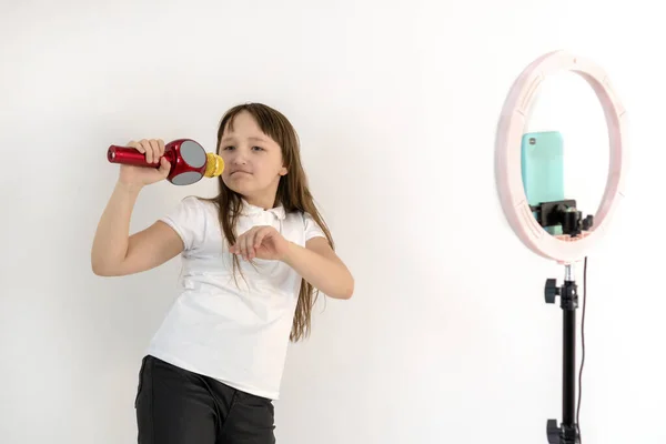 A teenage girl with a microphone in her hand sings and shoots a video. Selfies. The phone is mounted on a tripod and the ring lamp shines. Emotions Girl blogger — Stock Photo, Image