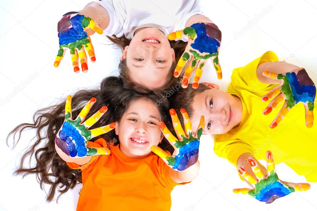 Three happy and smiling children are looking at the camera and holding out their hands in paints. Rainbow on the hands. The concept of a happy childhood and childrens day