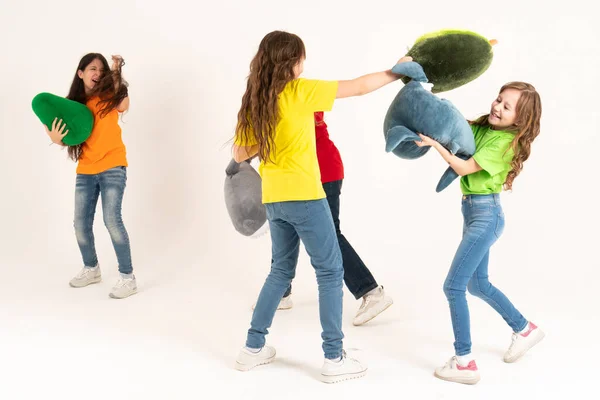 A group of children in bright clothes with their favorite soft toys beat each other like pillows on a white background. Studio photo. Childrens modern trend soft toy avocado and shark — Stock Photo, Image