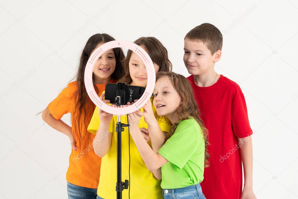 Three teen girls and a boy smiling and shoots a video. Selfies. The phone is mounted on a tripod and the ring lamp shines.