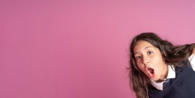 Uzun kıvırcık siyah saçlı, okul üniformalı ağzı zevkle açık çekici bir kız. Yüzünde haz ve şaşkınlık hissi var. Stüdyo fotoğrafı. Okula geri dön..