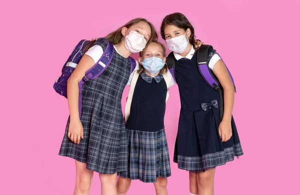 Три щасливі дівчата з довгим волоссям у шкільній формі носять медичні маски. Зупинити коронавірус. Дистанційне навчання. Студійне фото. Назад до школи — стокове фото