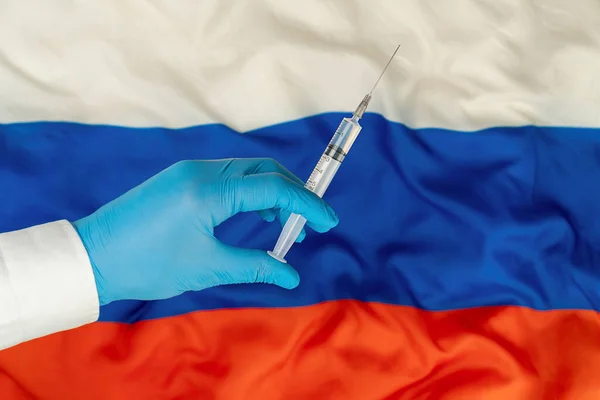 La siringa con un vaccino è tenuta a mano in un guanto sullo sfondo della bandiera della Federazione Russa, vaccino contro il coronavirus. — Foto Stock