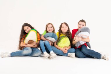 Beyaz arka planda en sevdikleri yumuşak oyuncakları ellerinde olan parlak elbiseli bir grup çocuk. Stüdyo fotoğrafı. Bebek modern trend yumuşak oyuncak avokado ve köpekbalığı.