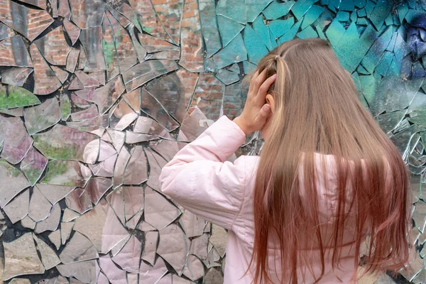 Young girl looks in a broken mirror