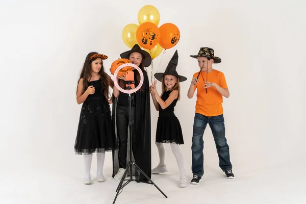 Tres chicas adolescentes y un niño sonriendo y filma un video. Selfies. El teléfono está montado en un trípode y la lámpara del anillo brilla. Niños y redes sociales. Emociones. —  Fotos de Stock