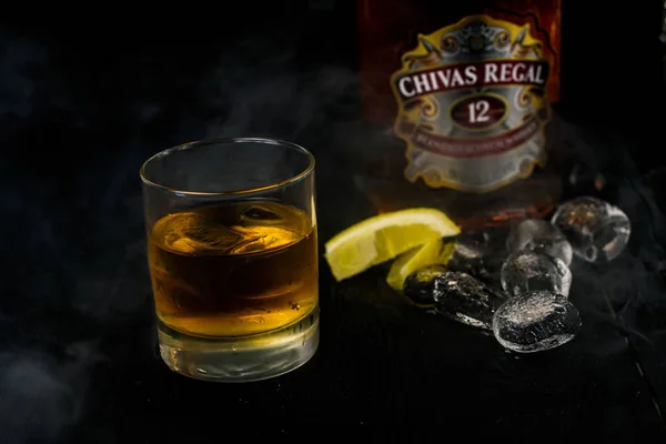 USA, Washington-26 marzo 2019. Una bottiglia di whisky Chivas Regal e un bicchiere di whisky con ghiaccio cubico su fondo di legno scuro, limone con ghiaccio — Foto Stock