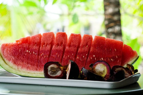 Fresh, ripe, striped sliced watermelon with mangosteen on a plate and a view of the palm trees. — Stock Photo, Image