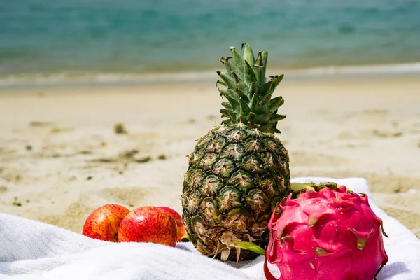 Frutas tropicales exóticas en una playa de arena.Piña, manzanas, fruta del dragón en la arena.Vista al mar . — Foto de Stock