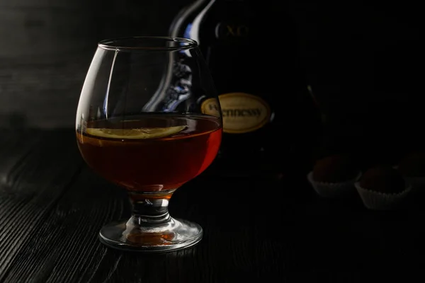 Hongkong, Hong Kong, mei 10, 2019: Cognac Hennessy X. O. 750 ml. glas met cognac, citroen schijfjes en chocolade truffel, staande op de tafel op een donkere houten achtergrond. — Stockfoto