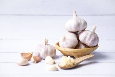 Sarımsak, dilimlenmiş sarımsak, sarımsak soğanı sepette karanfil bulunan beyaz renkli ahşap arka plan..