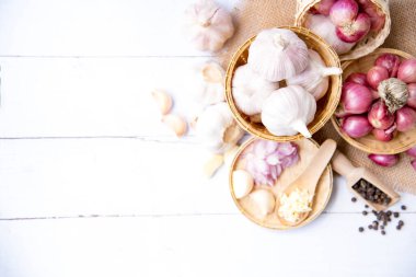 Sarımsak, soğan, karabiber, sarımsak, sarımsak karanfil, sarımsak soğanı, ahşap bir sepetin içinde beyaz ahşap bir sepet içinde soğan, bir bitki ve baharat karanfili veya yiyecek malzemeleri, yazı için yer, üst görüş. Sağlıklı gıda ya da bitkisel doğal tıp konsepti.