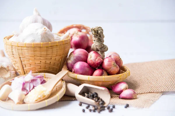 Garlic,shallot,Black pepper, fresh garlic, garlic clove, garlic bulb and Onion in a wooden basket on white wooden table, A herb and spice cloves or food ingredients, Place for text.