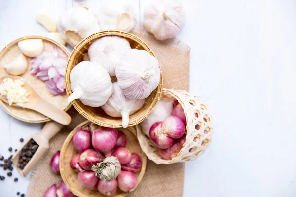 Garlic,shallot,Black pepper, fresh garlic, garlic clove, garlic bulb and Onion in a wooden basket on white wooden table, A herb and spice cloves or food ingredients, Place for text, top view. Healthy food or herbal natural medicine plant concept.