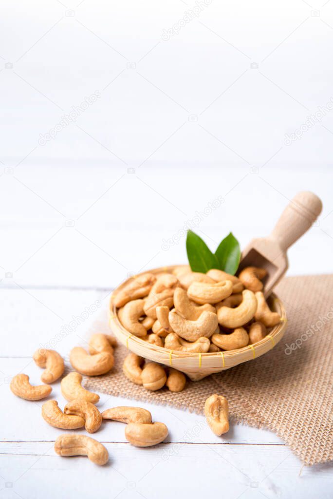 Cashew nuts with green leaves in basket and spoon isolated on white wooden background, selective focus, Healthy food