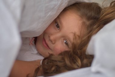 Battaniyenin altından bakan küçük bir kız. Saklambaç. Mutlu çocukluk konsepti.portre.