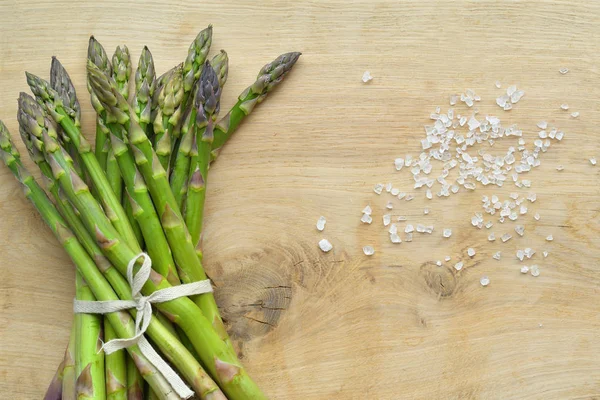 Bouquet d'asperges fraîches avec du gros sel de mer sur fond de bois. végétalisme et les aliments crus — Photo