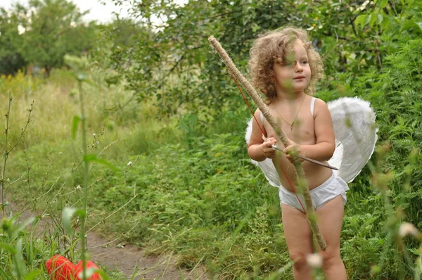 Kudrnaté dítě s křídlama z luku v červeném srdci. Valentýnský koncept — Stock fotografie