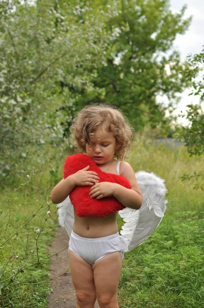 Chica rizada con alas sosteniendo un corazón rojo en sus manos. Concepto de San Valentín. humor romántico. Primavera — Foto de Stock