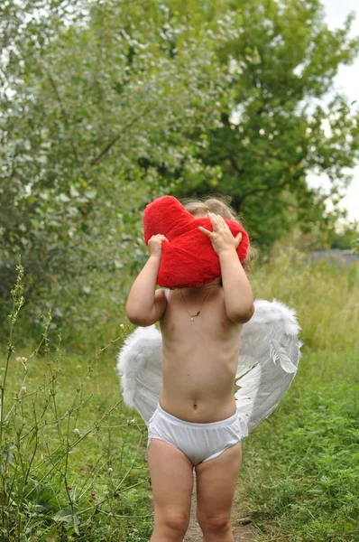 Chica rizada con alas sosteniendo un corazón rojo en sus manos. Concepto de San Valentín. humor romántico. Primavera — Foto de Stock