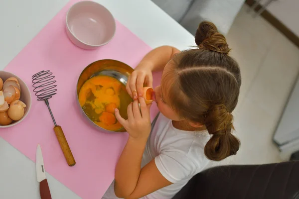 Маленькая девочка готовит печенье дома на кухне. У девушки вкус сырых яиц. Кулинария homemade food.Cooking is fun . — стоковое фото