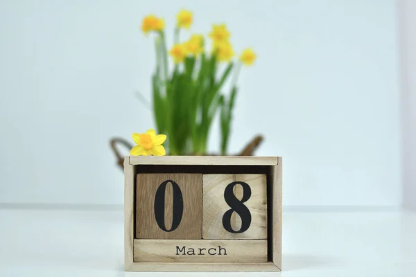 8 mars komposition på vit bakgrund. 8 mars text om trä block kalender och en blomma av gula narcissus .basket av påskliljor i bakgrunden — Stockfoto