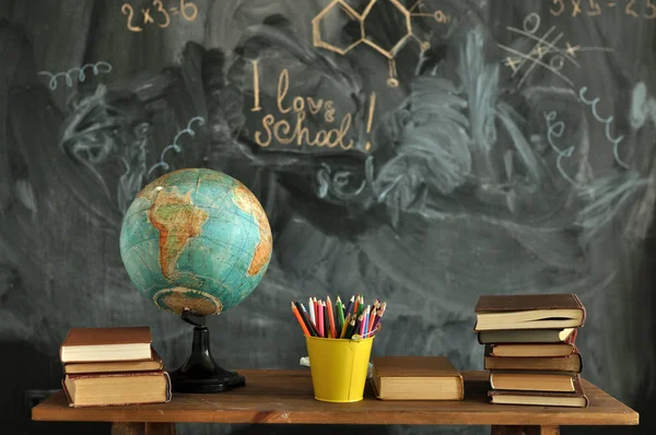 Materiałów szkolnych. Globe, kolorowe ołówki i książki na biurku. Zarząd szkoły w tle. — Zdjęcie stockowe