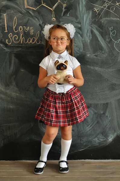 Cute girl in school uniform . Go to school for the first time. Girl indoors of the class room with blackboard on a background.back to school