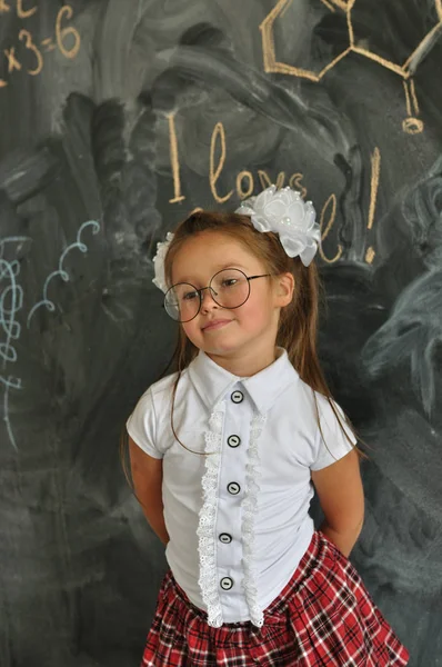 Cute Girl w mundurze szkolnym. Idź do szkoły po raz pierwszy. Dziewczyna w pomieszczeniu klasy z tablicy na tle. Powrót do szkoły — Zdjęcie stockowe