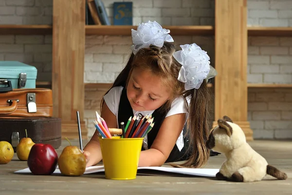 Cute Girl w szkole mundur z białymi kokardkami. ona leży na podłodze i czerpie z kolorowych ołówków — Zdjęcie stockowe