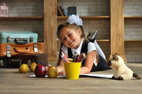 Cute Girl w szkole mundur z białymi kokardkami. ona leży na podłodze i czerpie z kolorowych ołówków — Zdjęcie stockowe