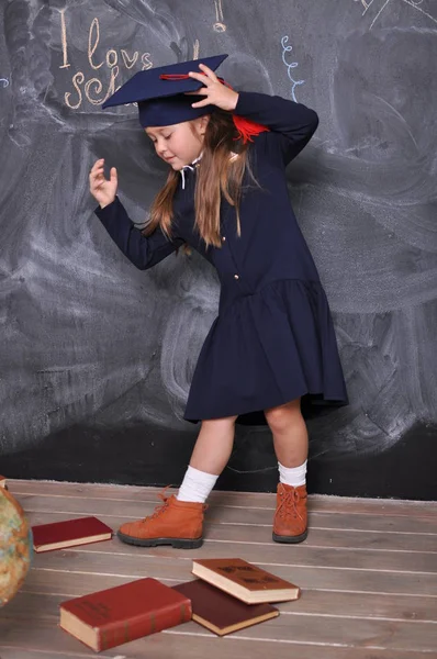 Portrait of a happy school girl standing in graduation hat.Go to school for the first time.Young girl exploring the globe.