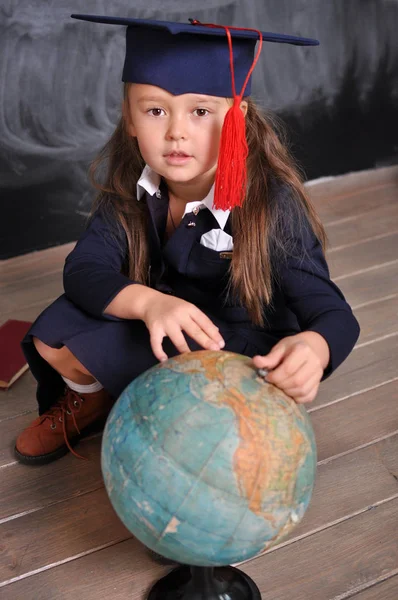 Portrait of happy school girl in graduation hat.Go to school for the first time.Young first-grade girl exploring the globe.school and education concept