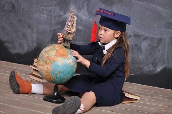 Portrait of happy school girl in graduation hat.Go to school for the first time.Young first-grade girl exploring the globe.school and education concept